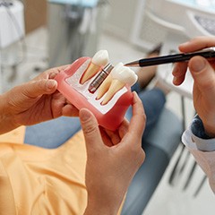 Dentist pointing to dental implant model held by dental patient
