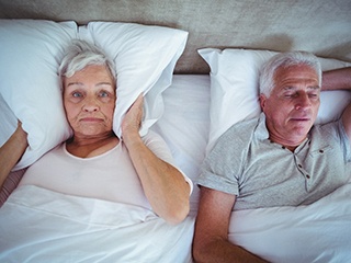 Senior man in gray shirt snoring, interrupting his wife’s sleep