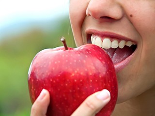 Closeup of woman biting into a red apple while outside