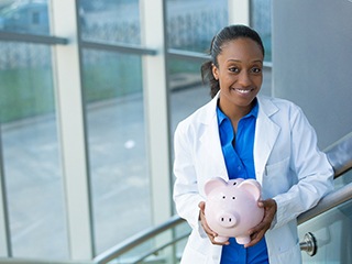 Smiling dentist holding piggy bank while wearing blue shirt