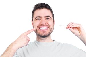 Man pointing at his teeth, enjoying benefits of Invisalign treatment