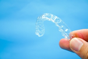 Close-up of Invisalign aligner held between fingers against blue background