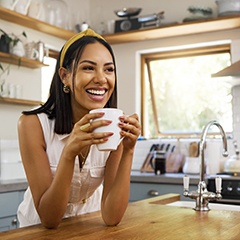 Woman smiling while drinking coffee in kitchen