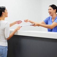 Smiling dental assistant handing patient form