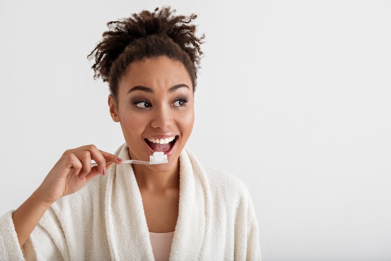 a woman wearing a robe and preparing to brush her teeth