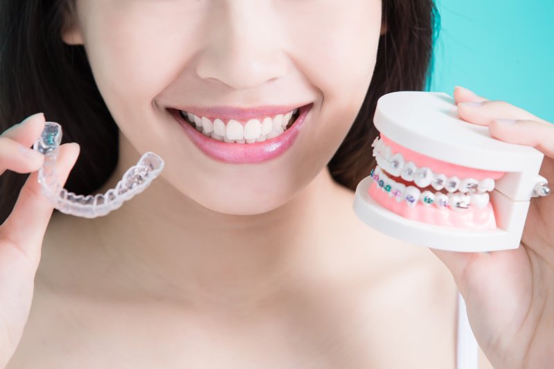 a woman holding a mouth mold with traditional braces as well as a clear Invisalign aligner