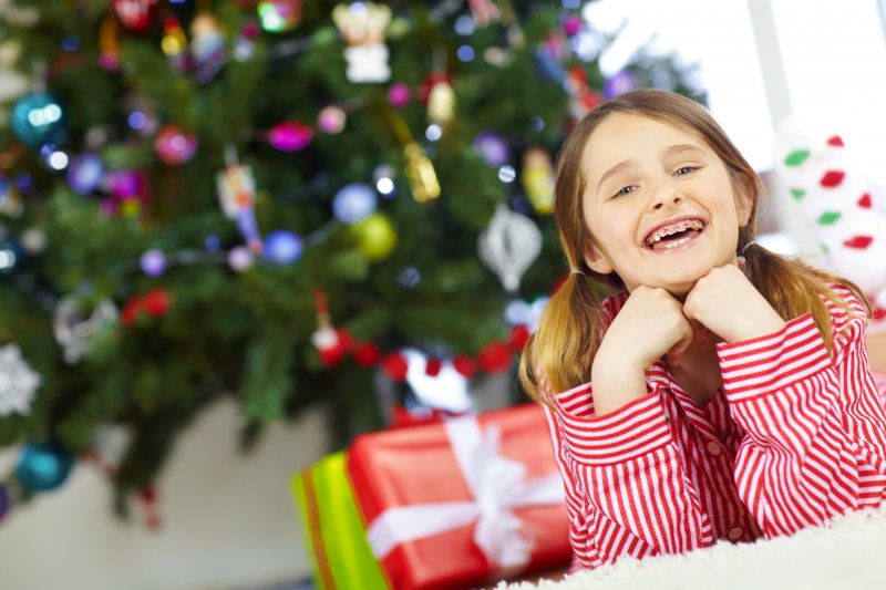 A child smiling by her holiday tree, pleased with her smile-friendly gifts