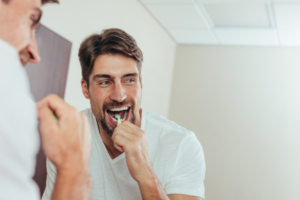 a person with dental implants smiling while brushing their teeth