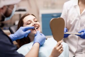 Patient in dentist's chair looking into handheld mirror while dentist prepares to place veneer.